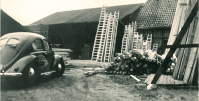 Historische foto van de DOLLE-groep, met klassieke voertuigen en industriële structuren.